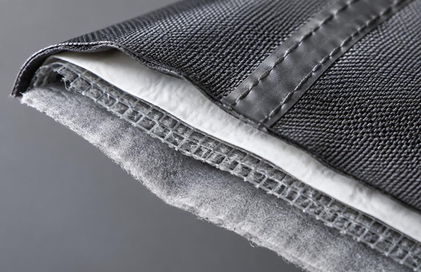 Cut edge of a five-layer cover fabric showing outer weave, membrane, scrim, fleece lining and taped seam